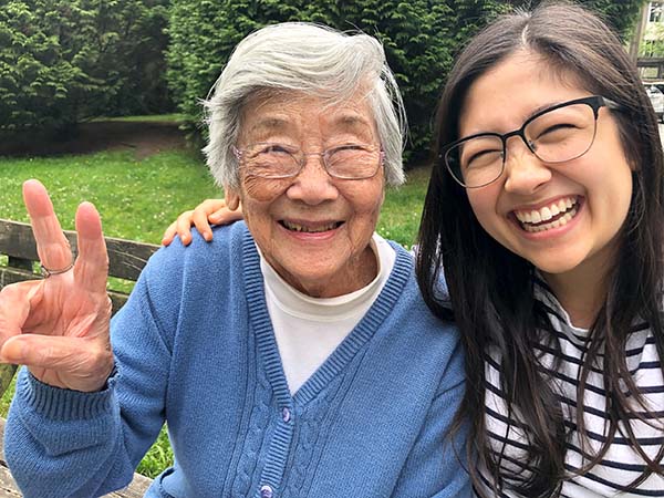 Happy Chinese grandma in her 90s making peace sign with granddaughter in her 20s outside in park.